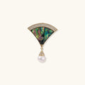 Gold fan-shaped brooch with iridescent abalone shell center, crystal border, and dangling white pearl on cream background