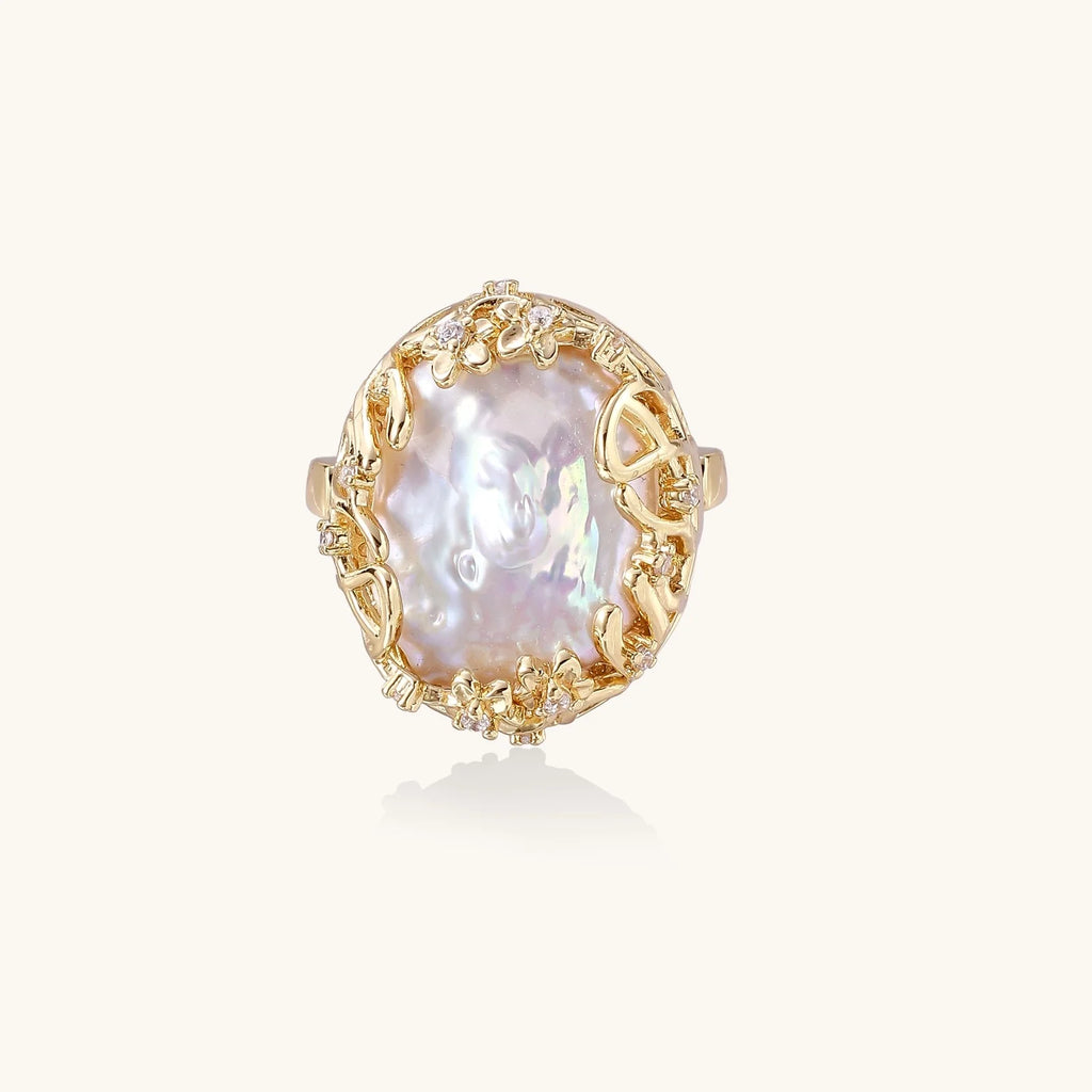 Gold filigree crown ring cradling an iridescent baroque freshwater pearl with crystal accents on white background