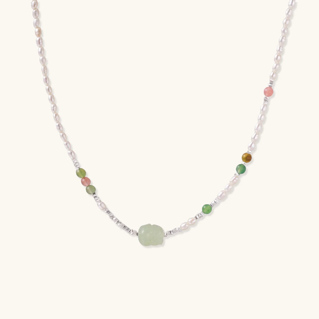 Delicate pearl necklace with pale green serpentine jade centerpiece and colorful agate beads on cream background