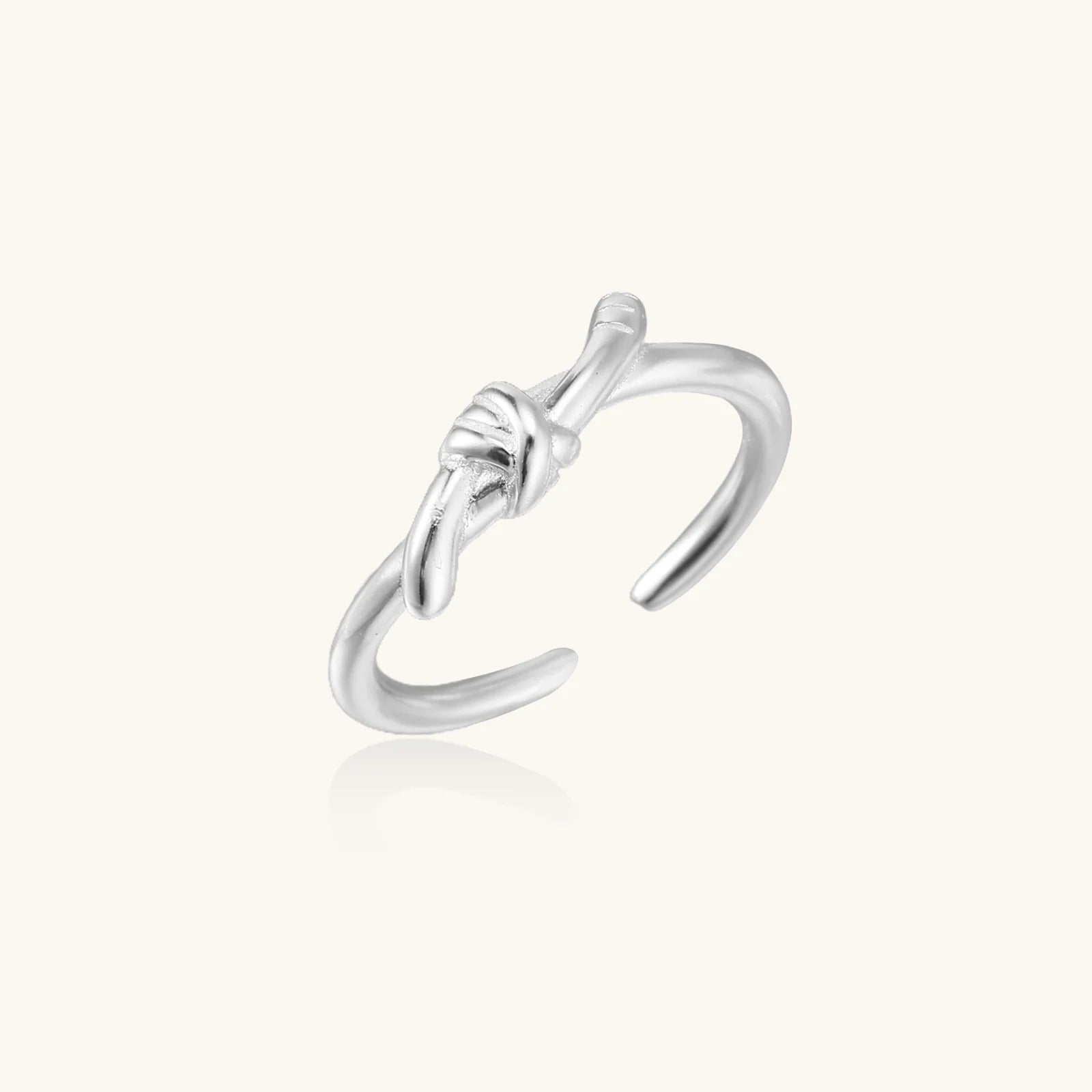 Delicate rhodium-plated silver ring with elegant knot design on cream background, adjustable band style
