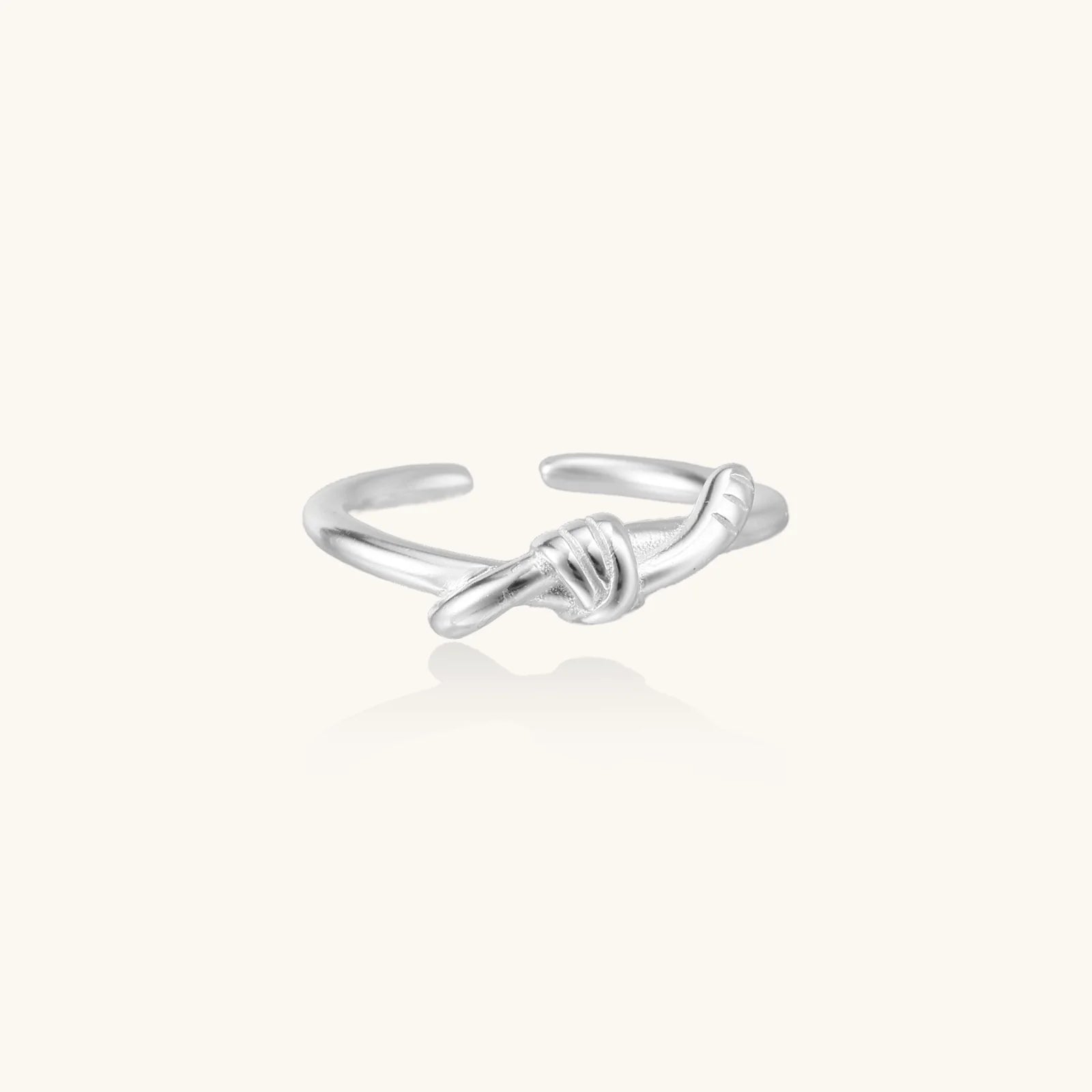 Delicate rhodium-plated silver ring with elegant knot design on cream background, adjustable band style