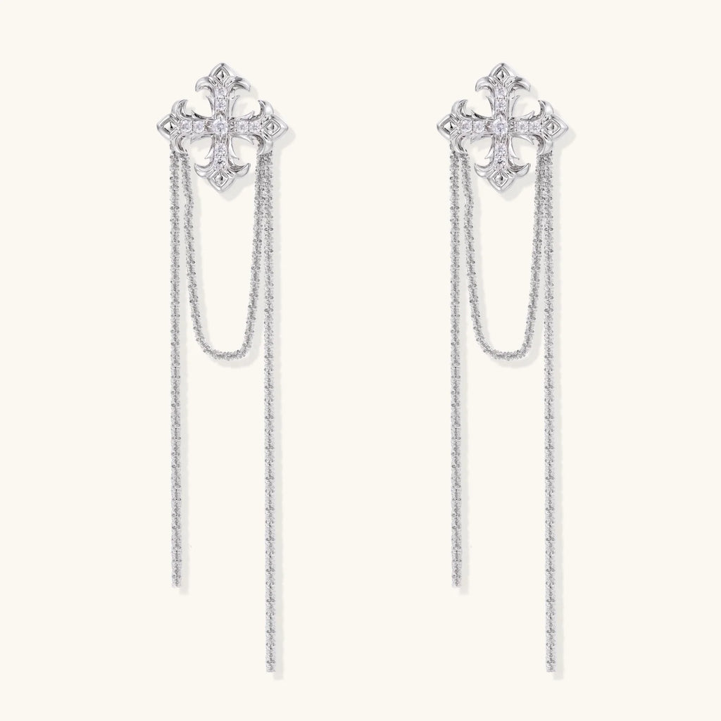 White gold plated baroque cross stud earrings with long cascading zirconia chains on cream background