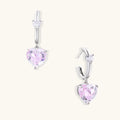 Silver huggie hoops with pink heart-cut zirconia pendants on white background, eco-friendly white gold plated brass