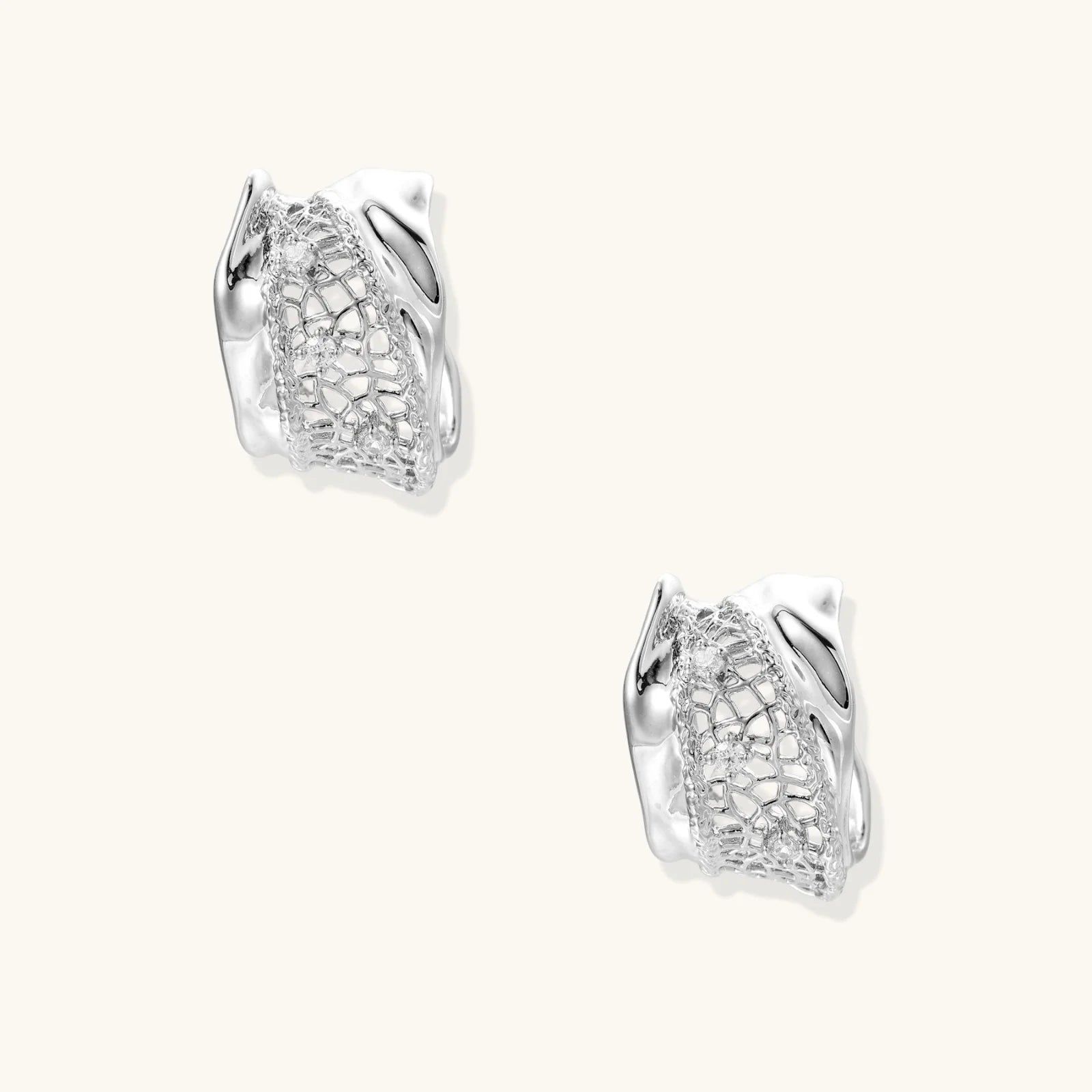 Close-up of sculptural hoop earrings with lattice center band and smooth twisted edges in white gold-plated brass with zirconia