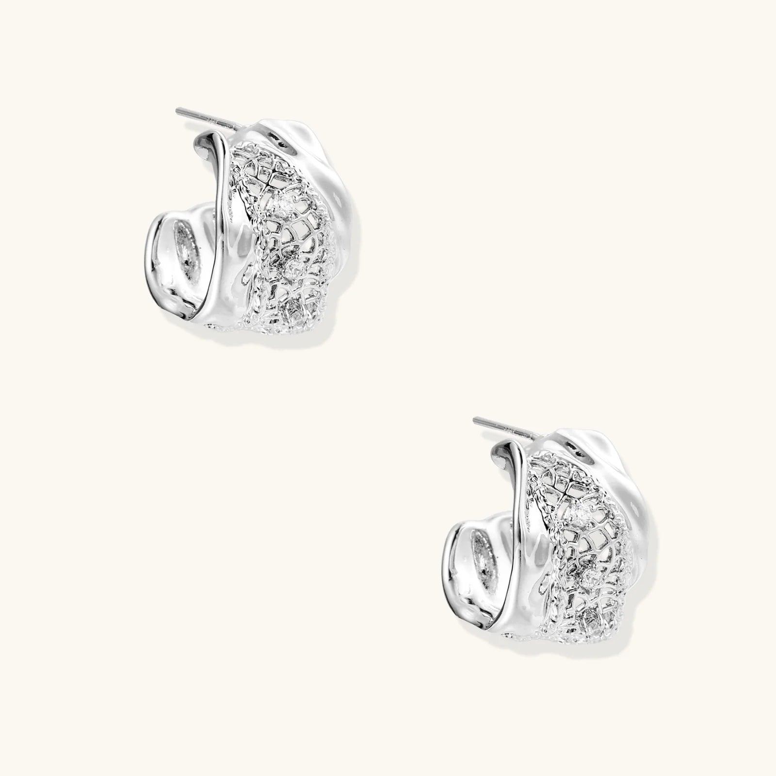 Close-up of sculptural hoop earrings with lattice center band and smooth twisted edges in white gold-plated brass with zirconia