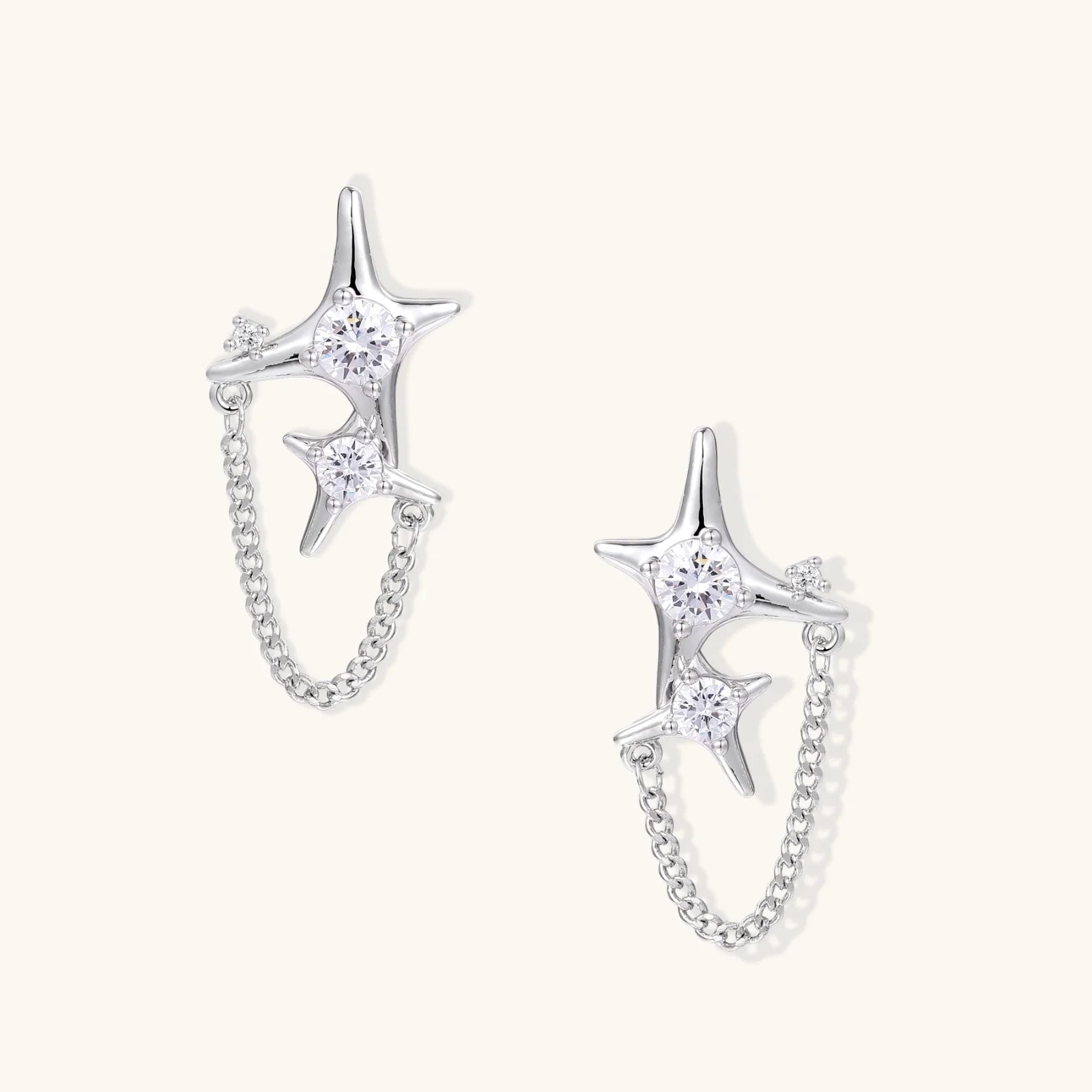 Silver star studs with crescent moon cutouts and zirconia stones connected by delicate chains on white background