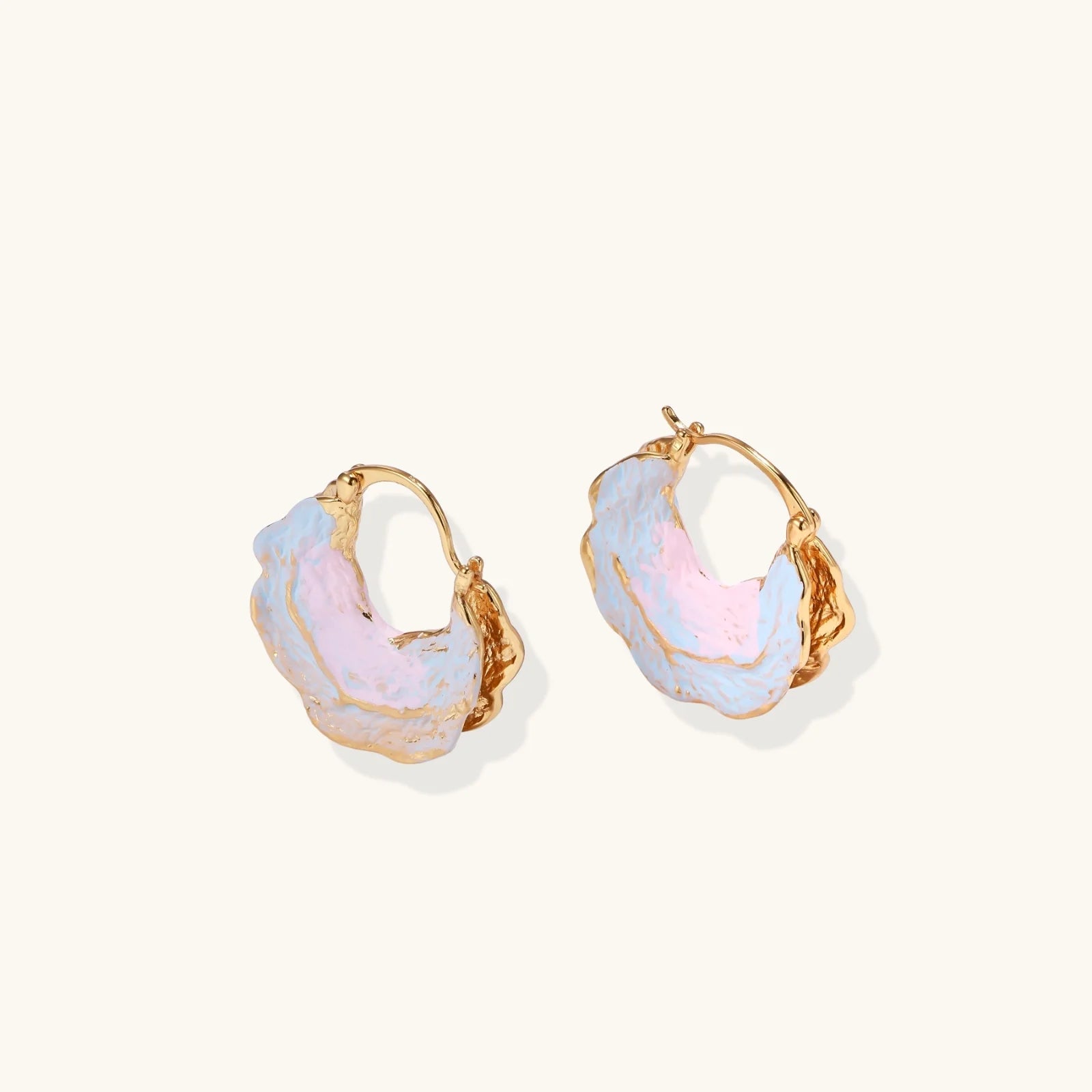 Shell-shaped hoop earrings with iridescent blue-pink enamel and gold trim on cream background