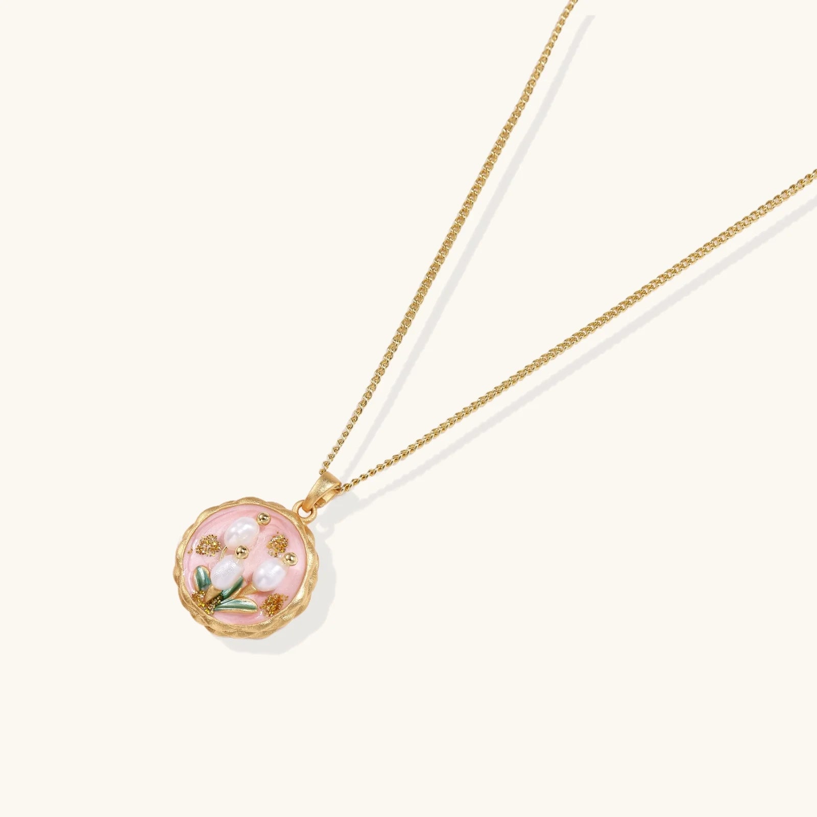 Gold pendant with pink enamel backdrop, white freshwater pearls as tulip blooms, and green leaf accents on rope chain.
