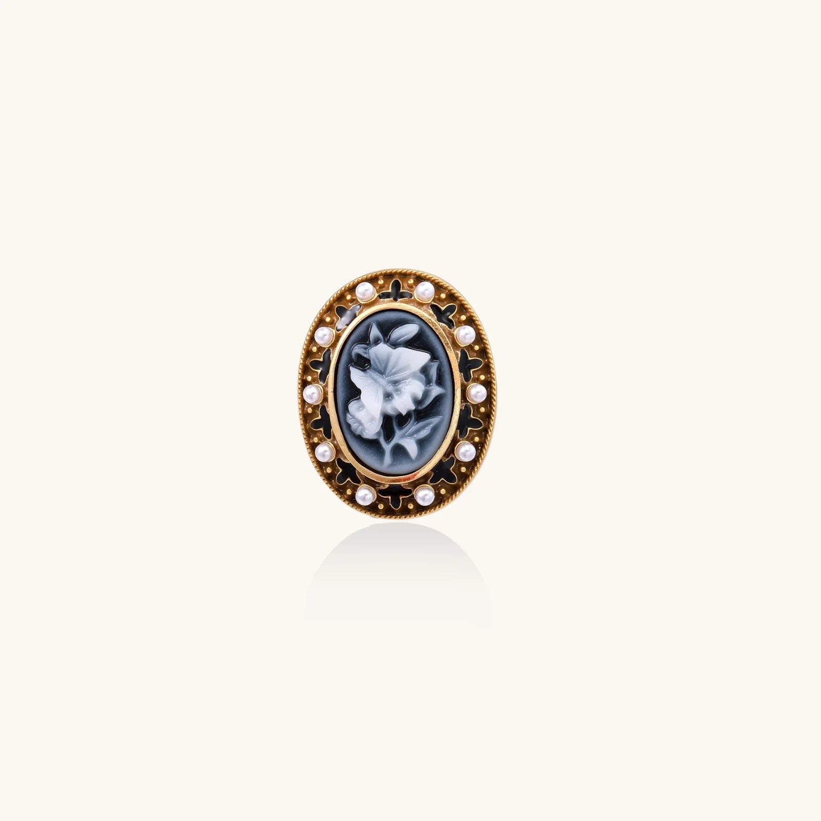 Gold-plated ring with oval blue floral cameo, pearl accents, and black enamel detailing on white background.