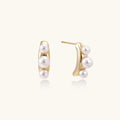 14K gold-plated curved stud earrings with three white freshwater pearls aligned vertically on cream background