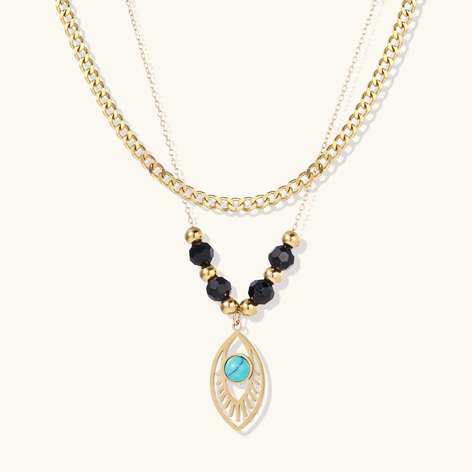 Layered gold necklace with turquoise evil eye pendant and black quartz beads on cream background