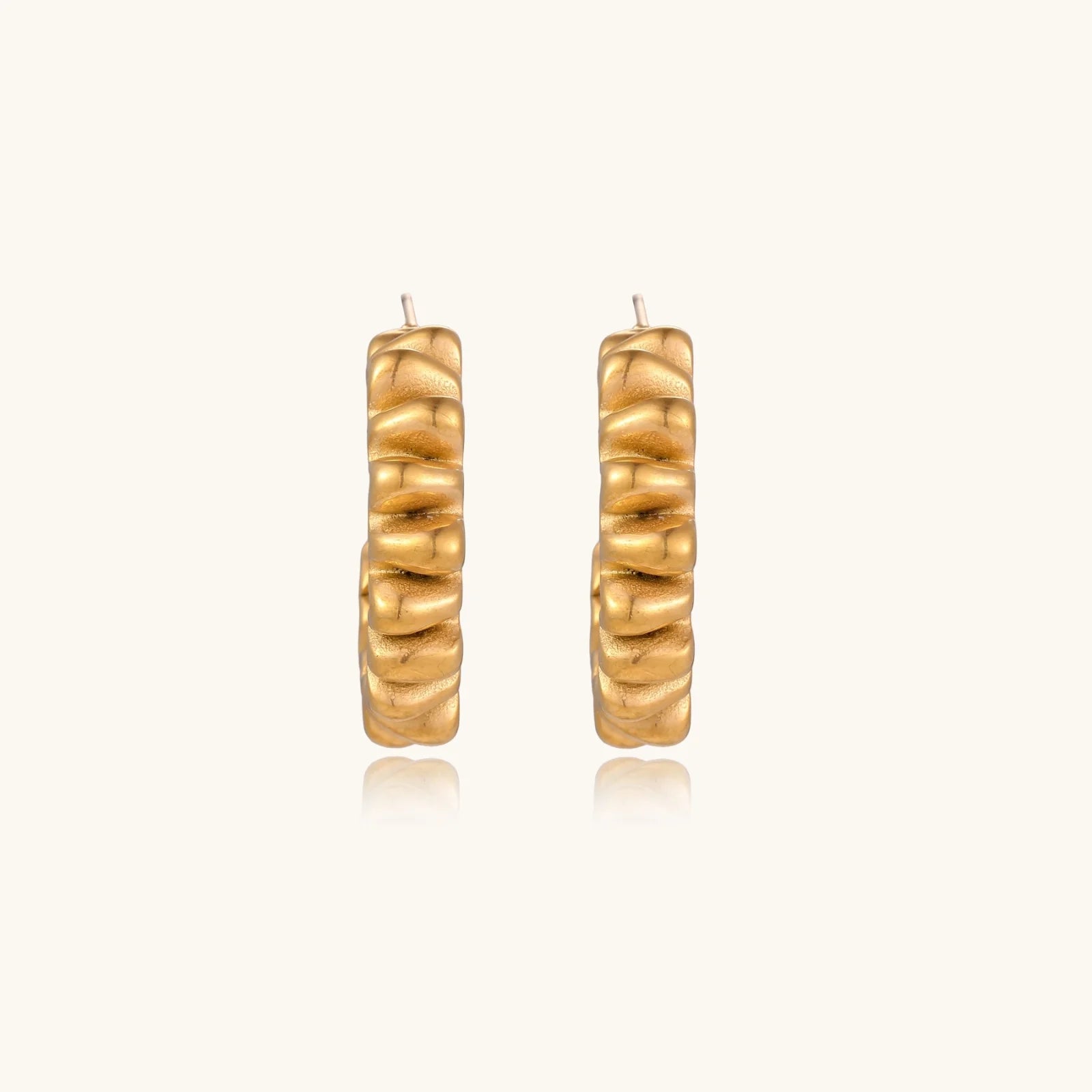 Sculptural gold-plated hoop earrings with continuous twisted spiral design on cream background
