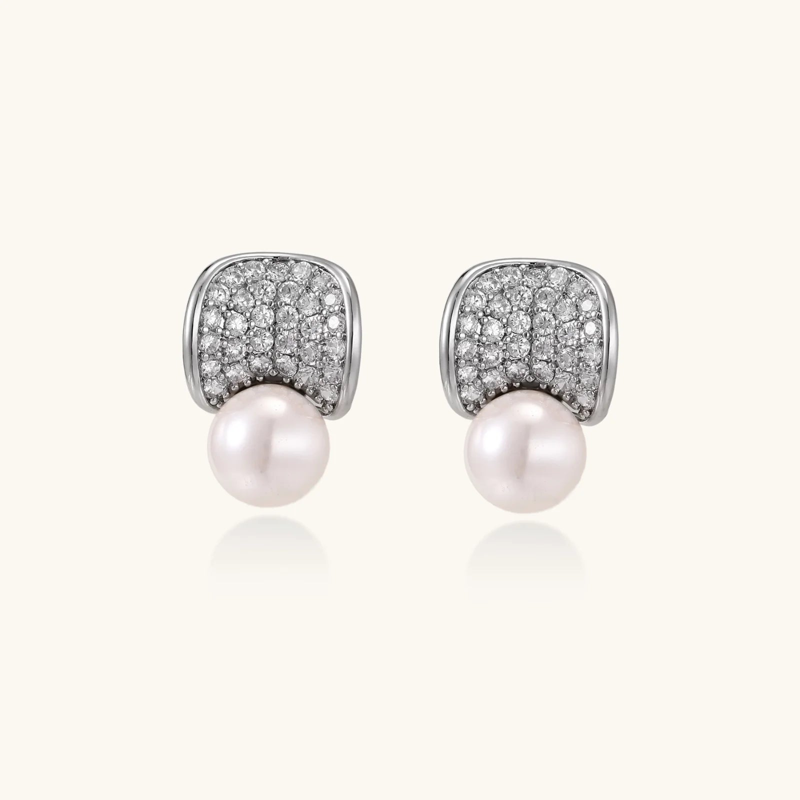 Curved pavé diamond studs in white gold-plated brass cradle lustrous freshwater pearls against cream background