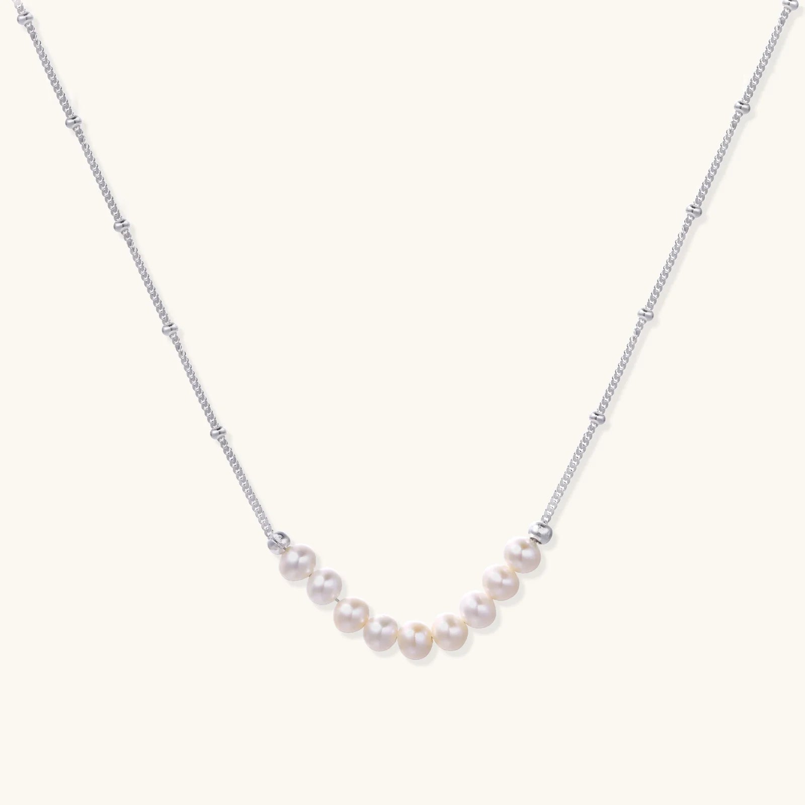 Delicate sterling silver chain necklace with small freshwater pearls arranged in a curved smile arc on cream background.